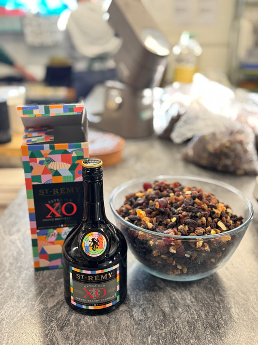 “A bottle of XO French brandy beside a bowl of mixed dried fruits, ready for soaking—ingredients for a traditional handmade wedding fruit cake.”