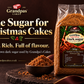 A 500g bag of Grandpas Cakes Dark Sugar displayed on a dark wooden surface next to a small bowl of the brown sugar. The background is a dark brown with promotional text reading 'The Sugar for Christmas Cakes'.