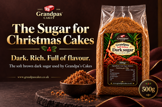 A 500g bag of Grandpas Cakes Dark Sugar displayed on a dark wooden surface next to a small bowl of the brown sugar. The background is a dark brown with promotional text reading 'The Sugar for Christmas Cakes'.