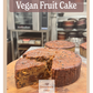 Vegan fruit cake on a wooden board with 'Grandpa's Cakes' branding in a bakery setting.